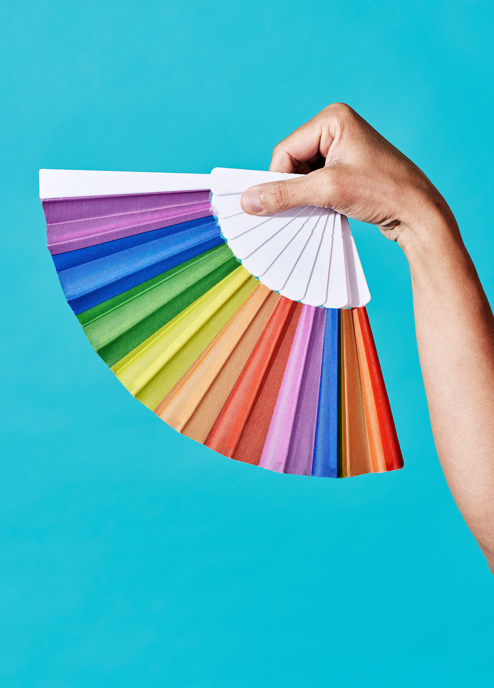 Isolated hand holding a rainbow fan in front of a bright blue background