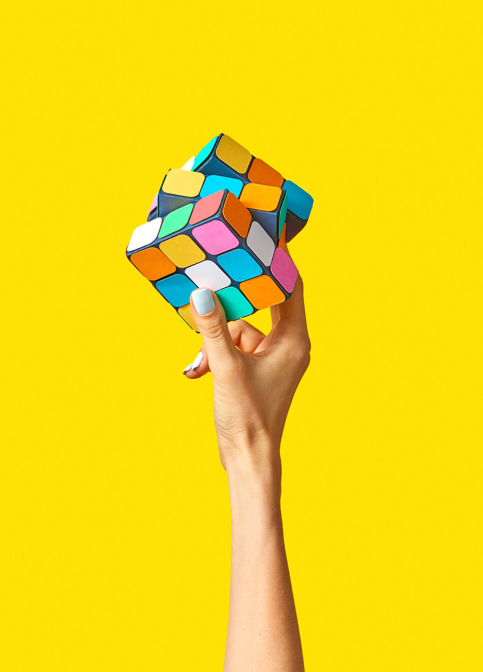 Isolated hand holding a rubik's cube in front of a bright yellow background