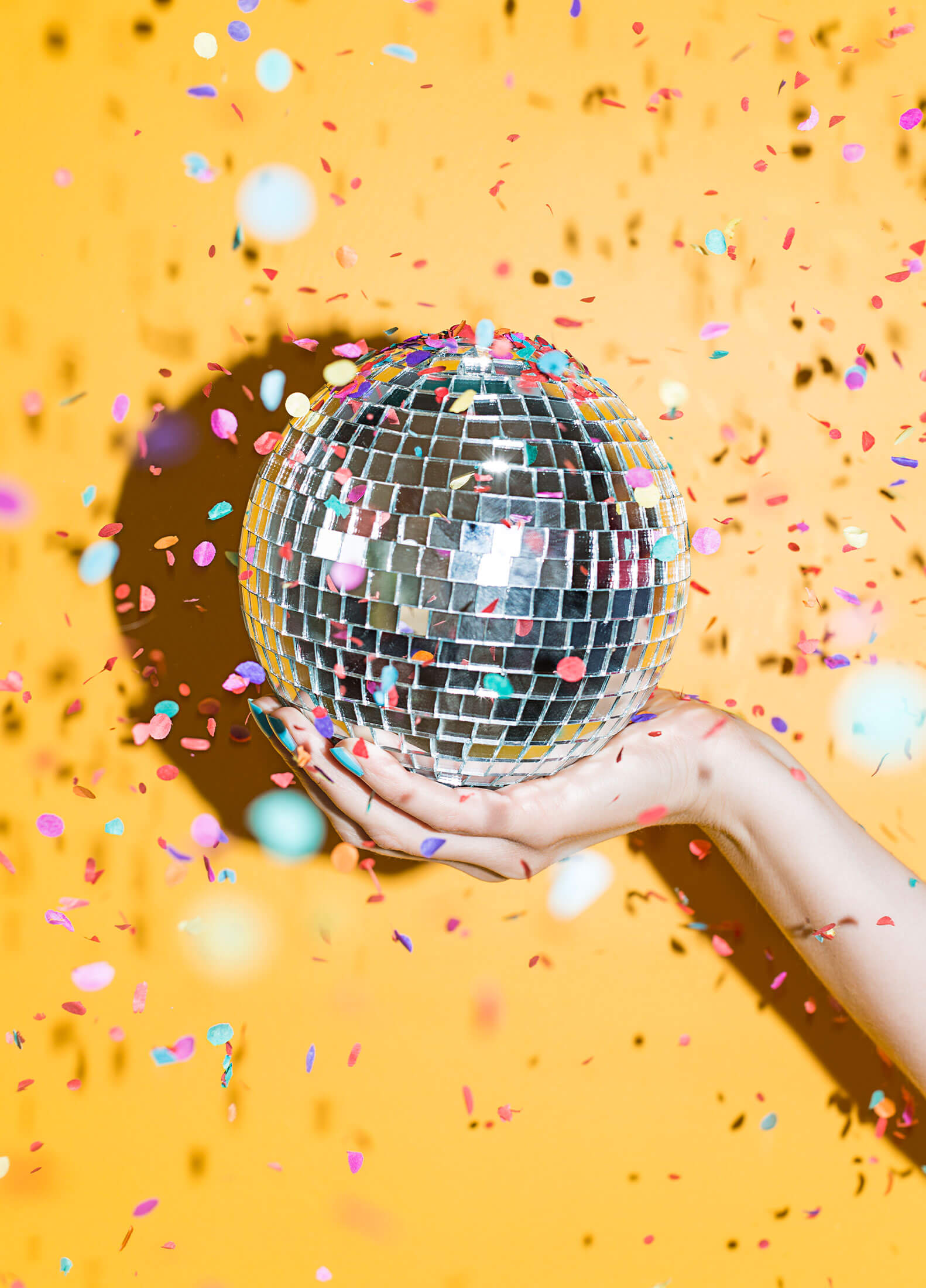 Isolated hand holding a disco ball in front of a bright yellow background
